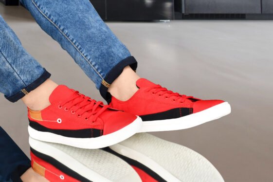 Men's red and black canvas sneakers with white soles, paired with blue denim jeans, showcasing a trendy fashion shoe style.