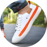 White canvas shoes for men - stylish and comfortable sneakers for casual wear. A close-up of a stylish men's sneaker in white with orange accents, worn with rolled-up denim jeans on an outdoor road.
