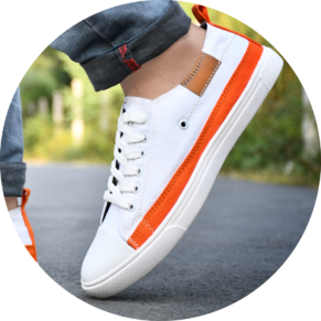 Home 2 31 White canvas shoes for men - stylish and comfortable sneakers for casual wear. A close-up of a stylish men's sneaker in white with orange accents, worn with rolled-up denim jeans on an outdoor road.